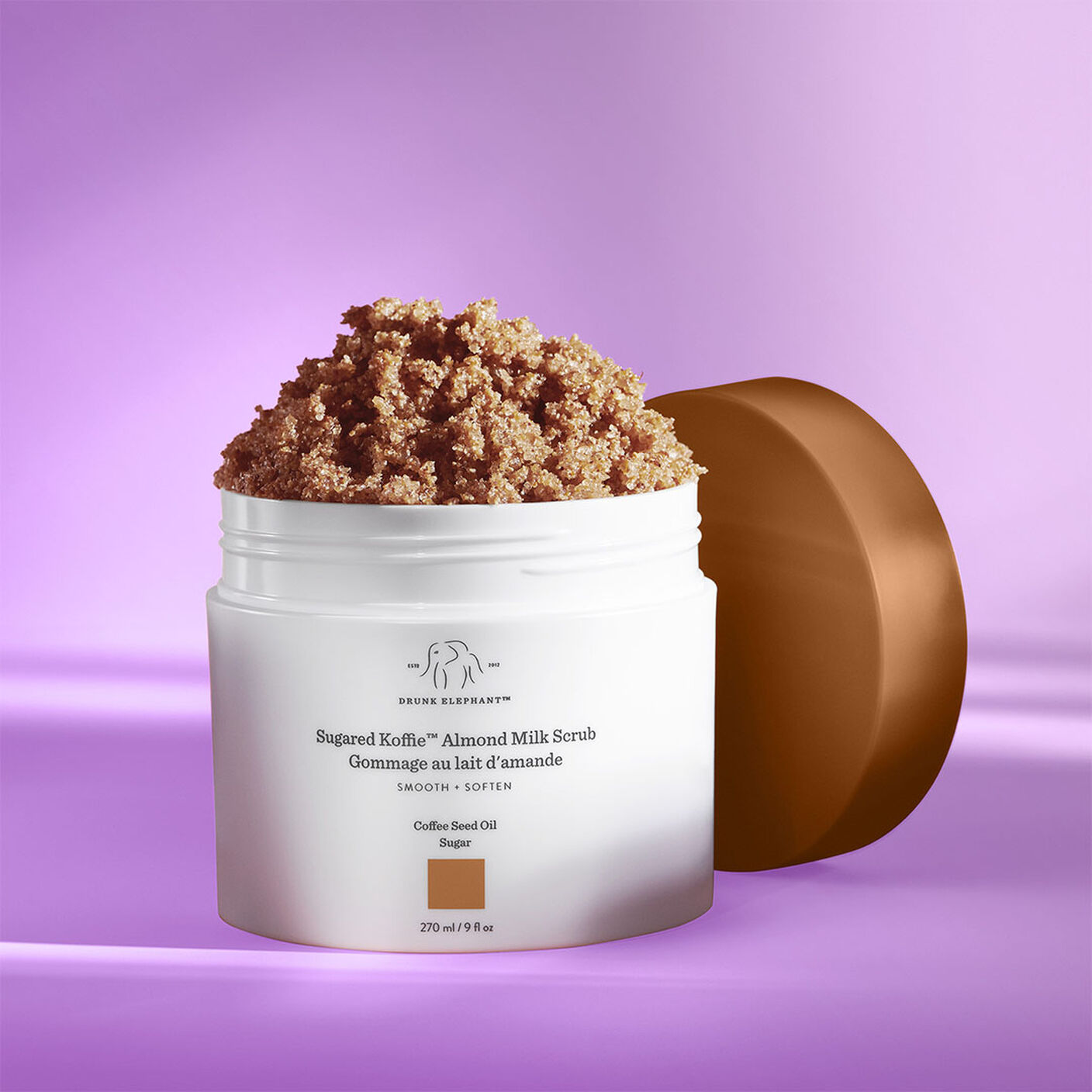 Sugared Koffie Almond Milk Body Scrub with the cap off on a purple table. 