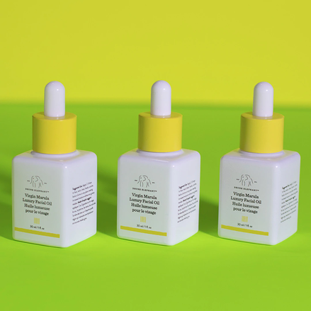 photo of three marula oil bottles aligned on a light green surface against a yellow background