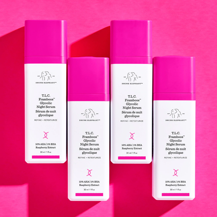photo of four TLC Framboos bottles lined up at alternating heights on a dark pink background