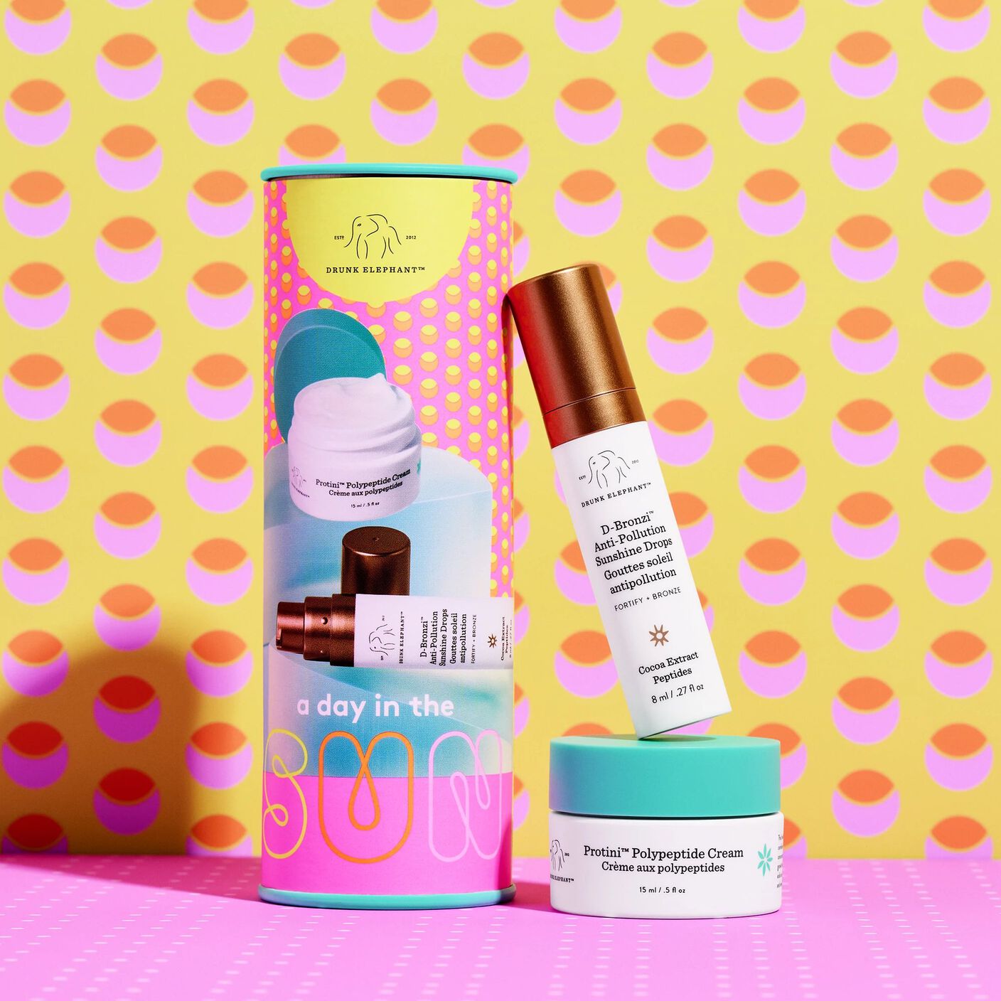  A Day in the Sun kit with D-Bronzi (8ml) and Protini Cream (15ml) beside it in front of a pink and prange polka dot background.