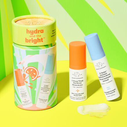 Cylinder packaging with 8ml B-Hydra and 9ml C-Firma fresh with texture sample on a yellow floor in front of a green neon striped background.