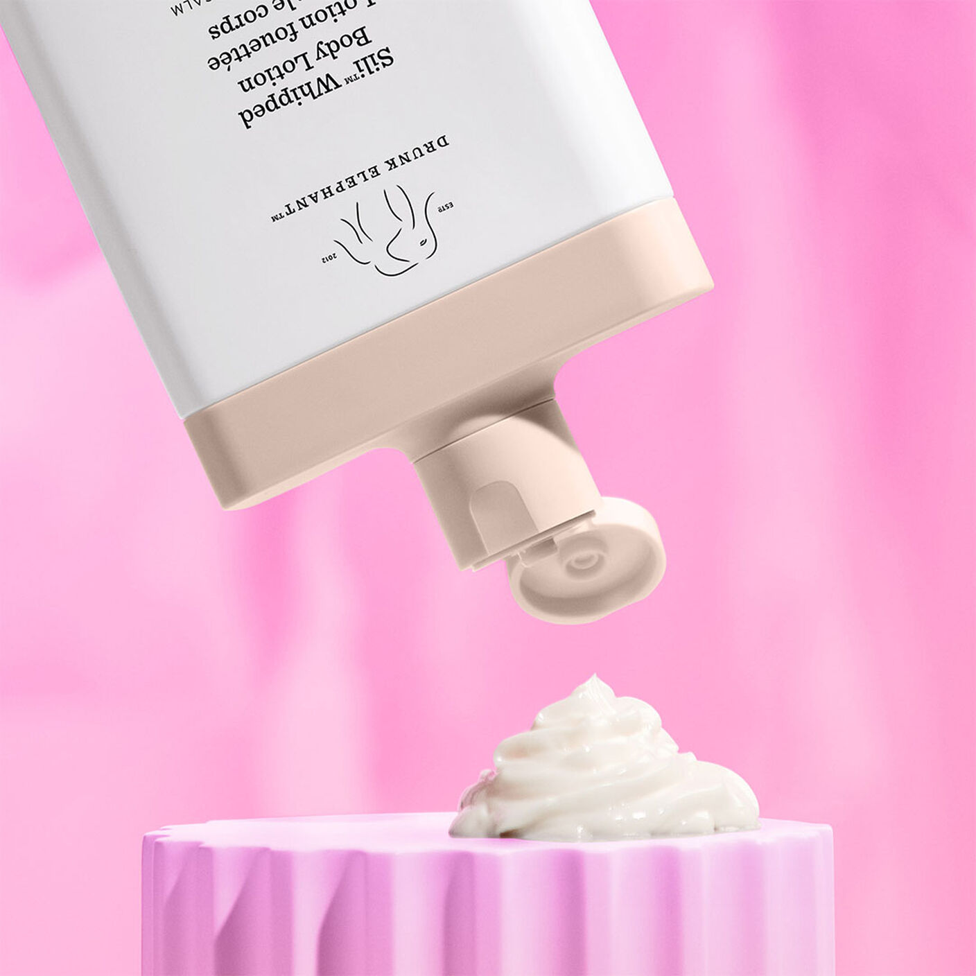 Sili Whipped Body Lotion being poured out onto a pink acrylic prop. 