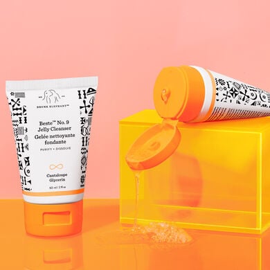 one Beste bottle standing and one Beste bottle laid flat on an orange acrylic box against a peach background