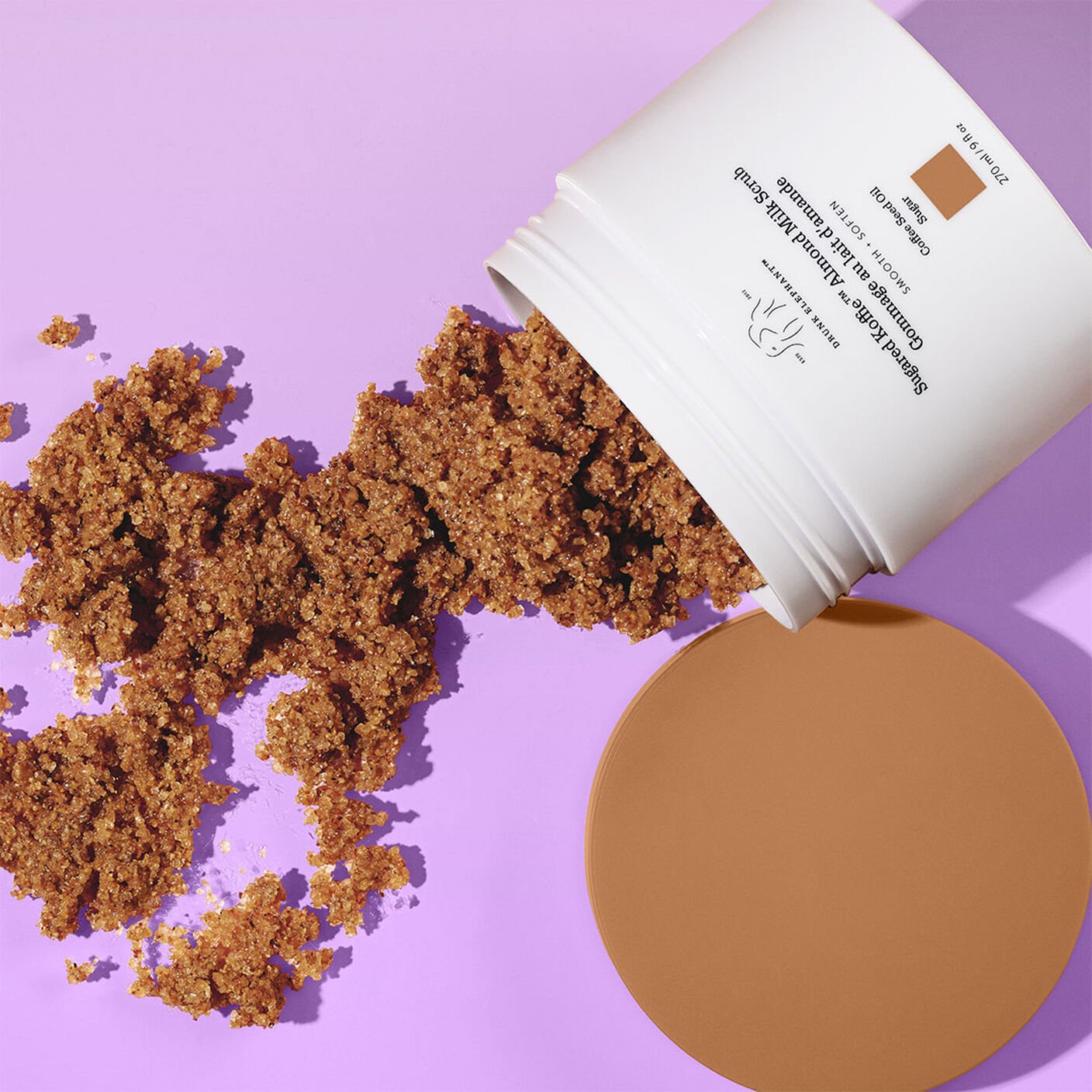 Sugared Koffie Almond Milk Body Scrub  poured out onto a putple table with the cap to the side. 